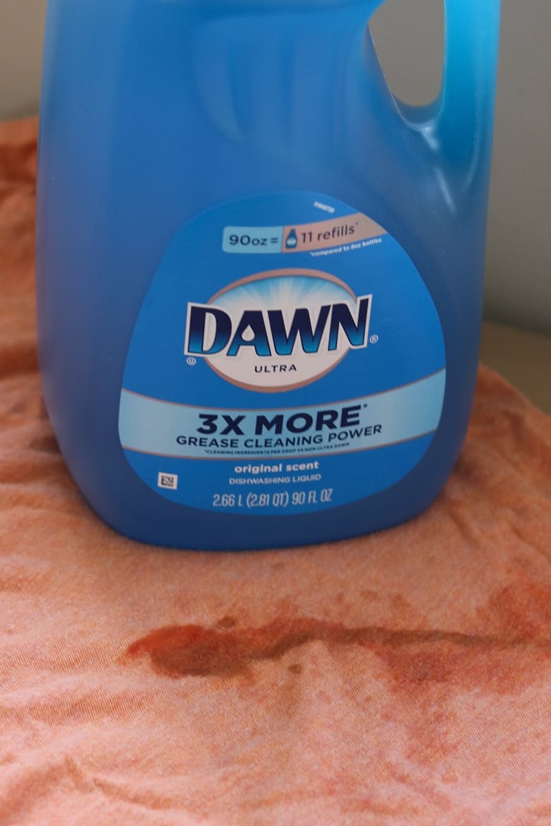 Container of blue Dawn dish soap on top of a stained orange shirt