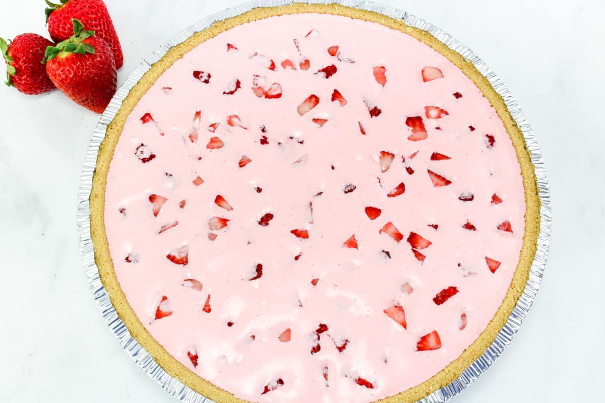 pink pie with strawberries in it in a graham cracker crust.