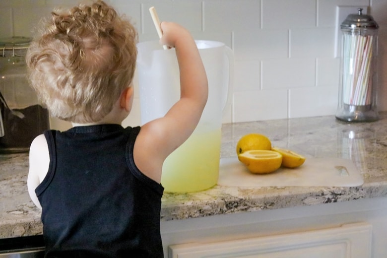 Toddler boy stirring a pitcher of lemonade. 