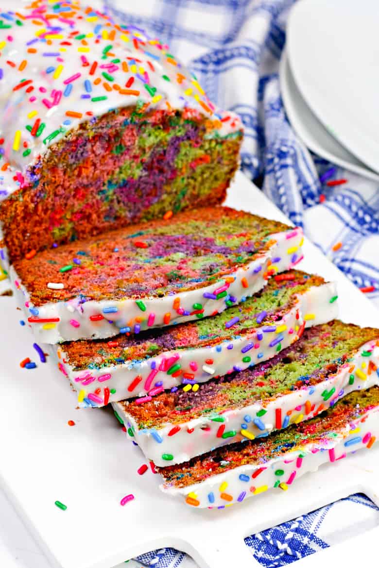Rainbow loaf of bread, covered in icing and rainbow sprinkles. Slices are cut from the loaf so that you can see in inside rainbow colors.