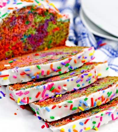Rainbow sprinkle covered iced unicorn quick bread, sliced to show the vibrant swirl of colors inside the loaf.