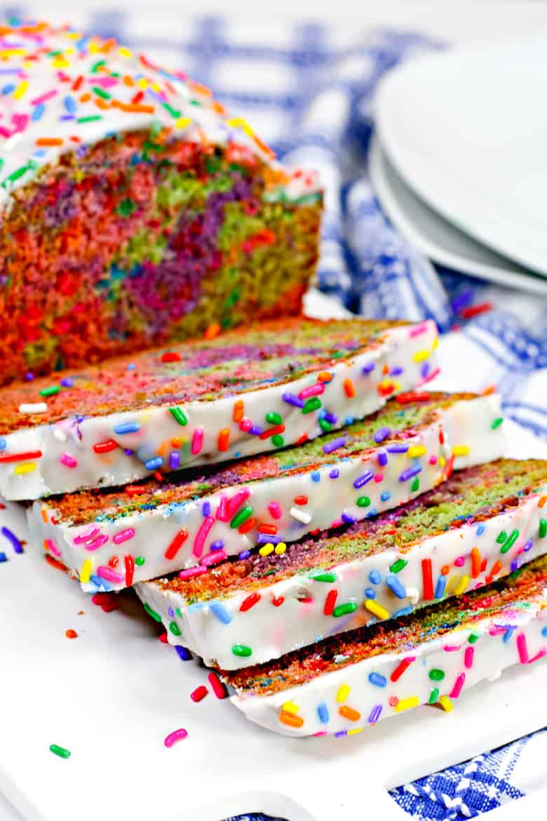 Rainbow sprinkle covered iced unicorn quick bread, sliced to show the vibrant swirl of colors inside the loaf.