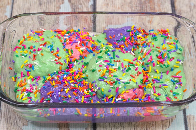 Purple, pink, and green batter in a 9 x 9 loaf pan, with sprinkles on top