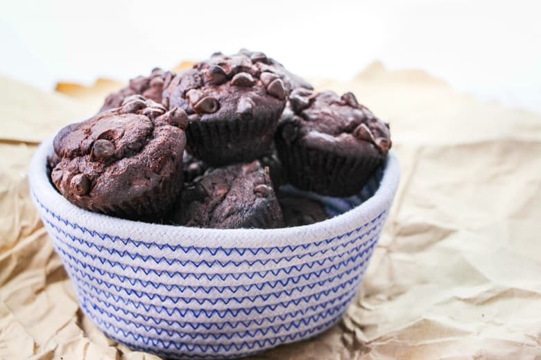 Blue and white woven bowl filled with chocolate muffins with chocolate chips.