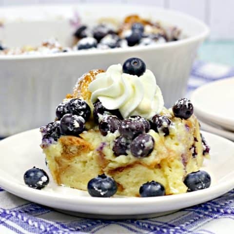 Slice of blueberry breakfast bake garnished with fresh blueberries and whipped cream