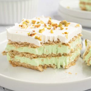 A slice of pistachio icebox cake with layers of graham crackers, green pistachio filling, and whipped topping, garnished with chopped pistachios.