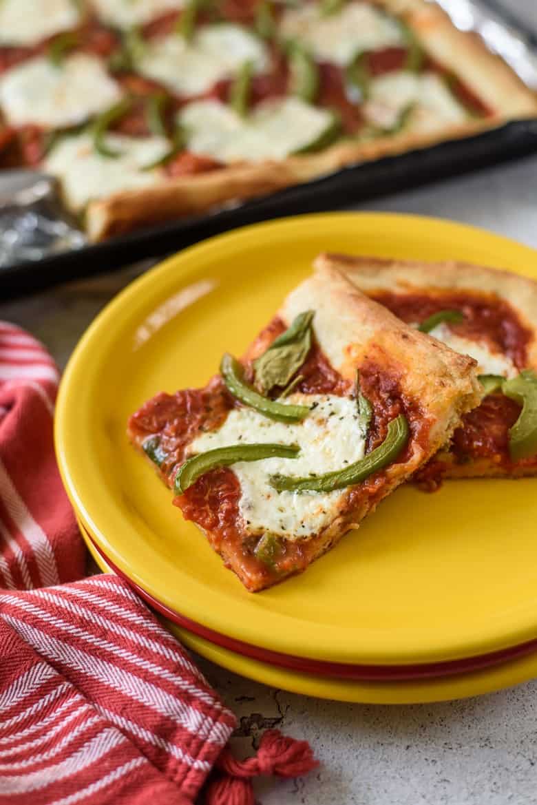 Two slices of pizza on yellow plate, with the rest of pizza in background