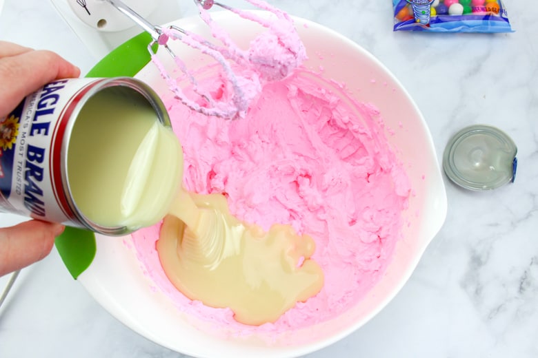 pouring can of sweetened condensed milk into bowl of pink whipped cream