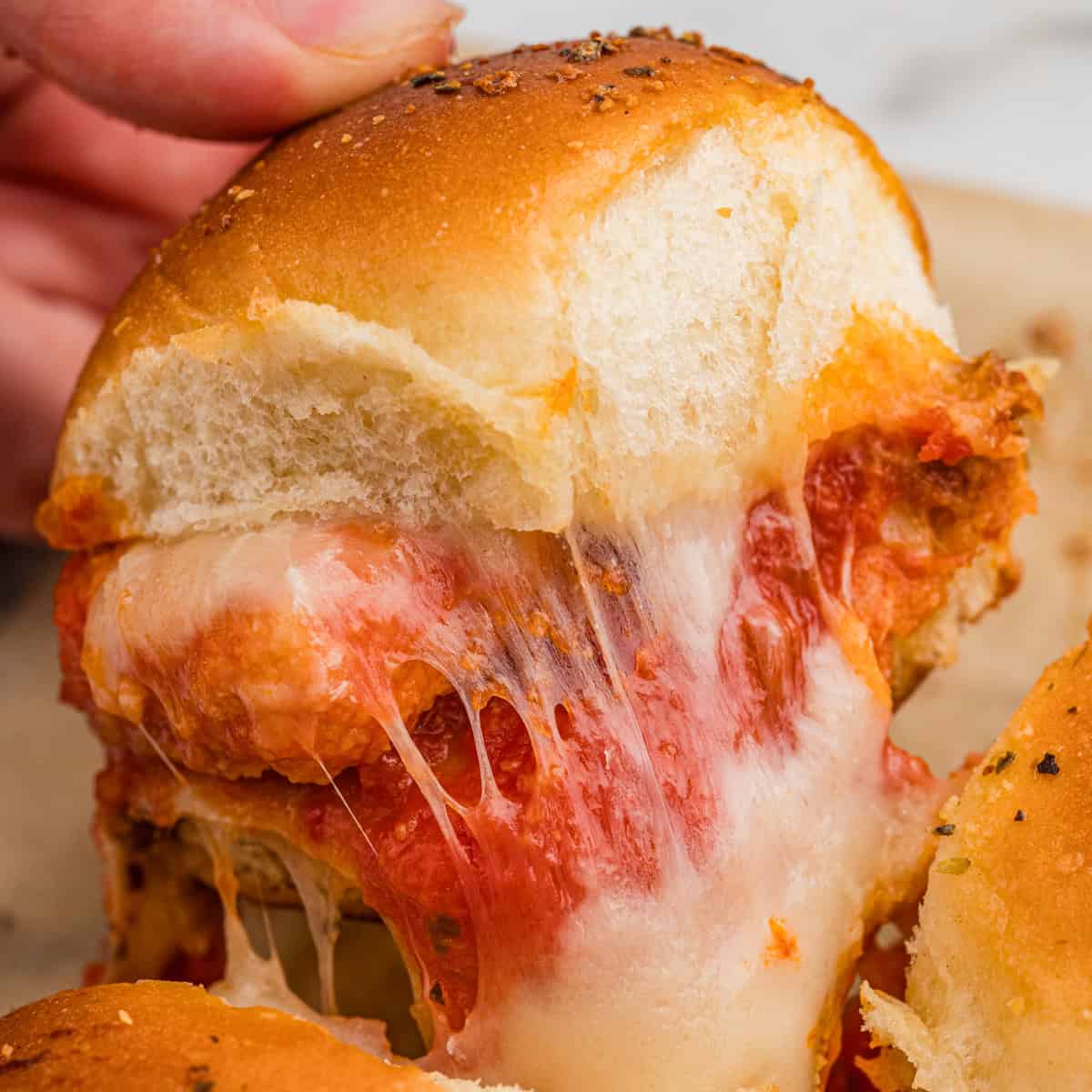 A chicken parm slider with nuggets and melty cheese being pulled from the pan.