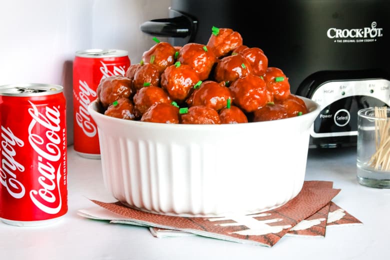 Coca-Cola Meatballs in white bowl with Crockpot and Coke cans