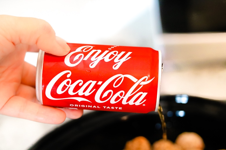 Hand pouring Coca-Cola can into crockpot