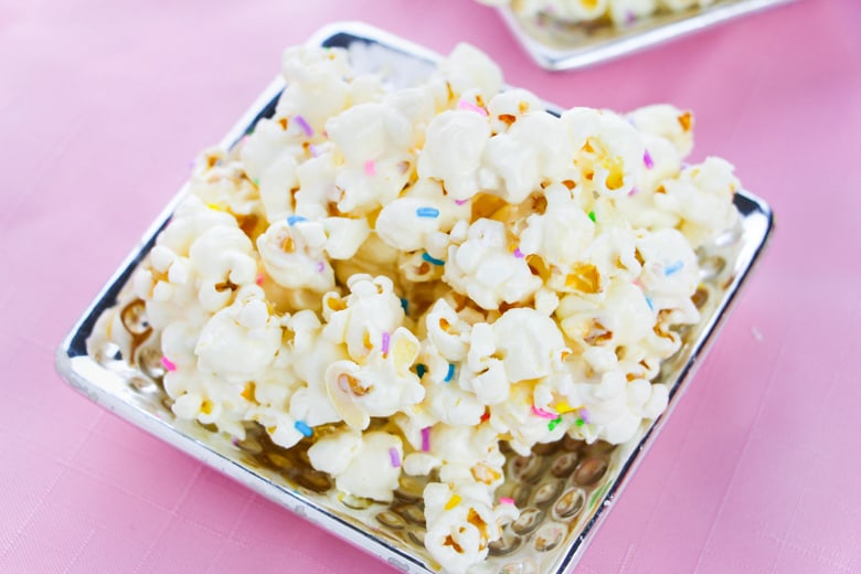 Cake batter popcorn topped with rainbow sprinkles and served on a flat silver plate.