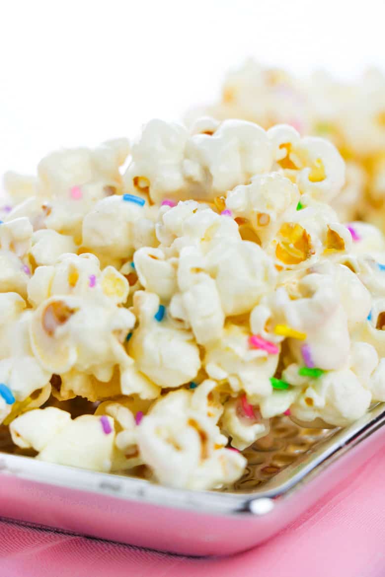 Cake batter popcorn topped with rainbow sprinkles and served on a flat silver plate.