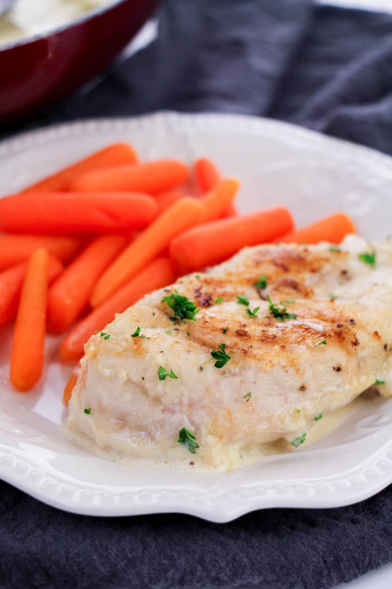 Chicken breast in a creamy sauce and cooked mini carrots on a white dinner plate.