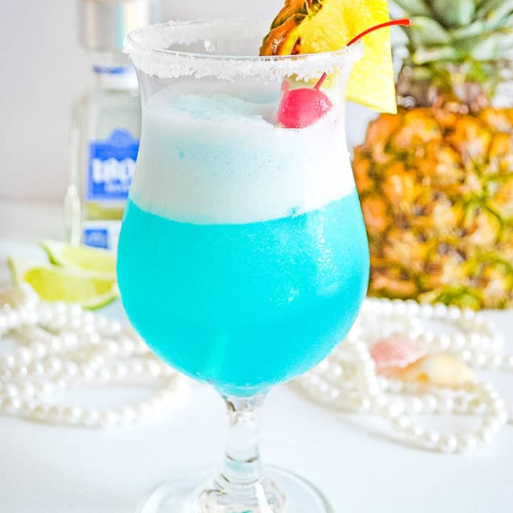 Frozen blue cocktail garnished with fresh pineapple and maraschino cherry