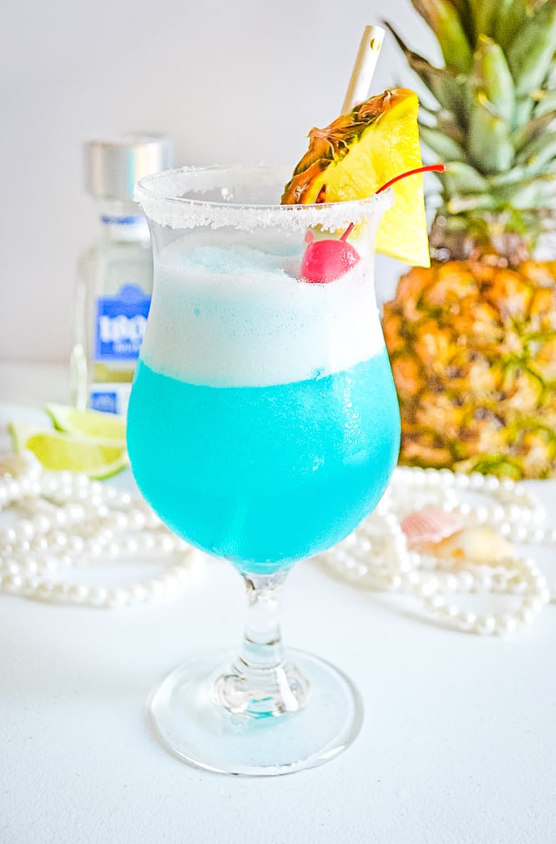 Frozen blue cocktail garnished with fresh pineapple and maraschino cherry