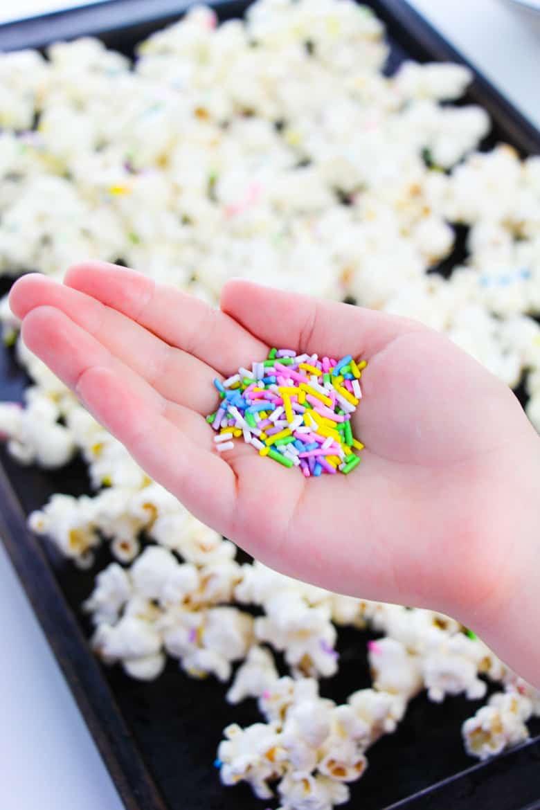 Woman's hand holding sprinkles over tray of popcorn