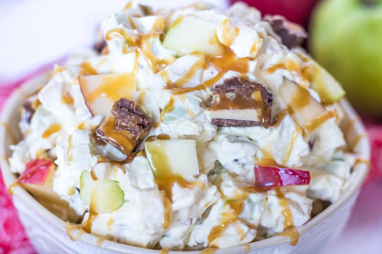 Apple snicker salad in a white bowl with chunks of candy bars, red and green apples, and a creamy dressing.