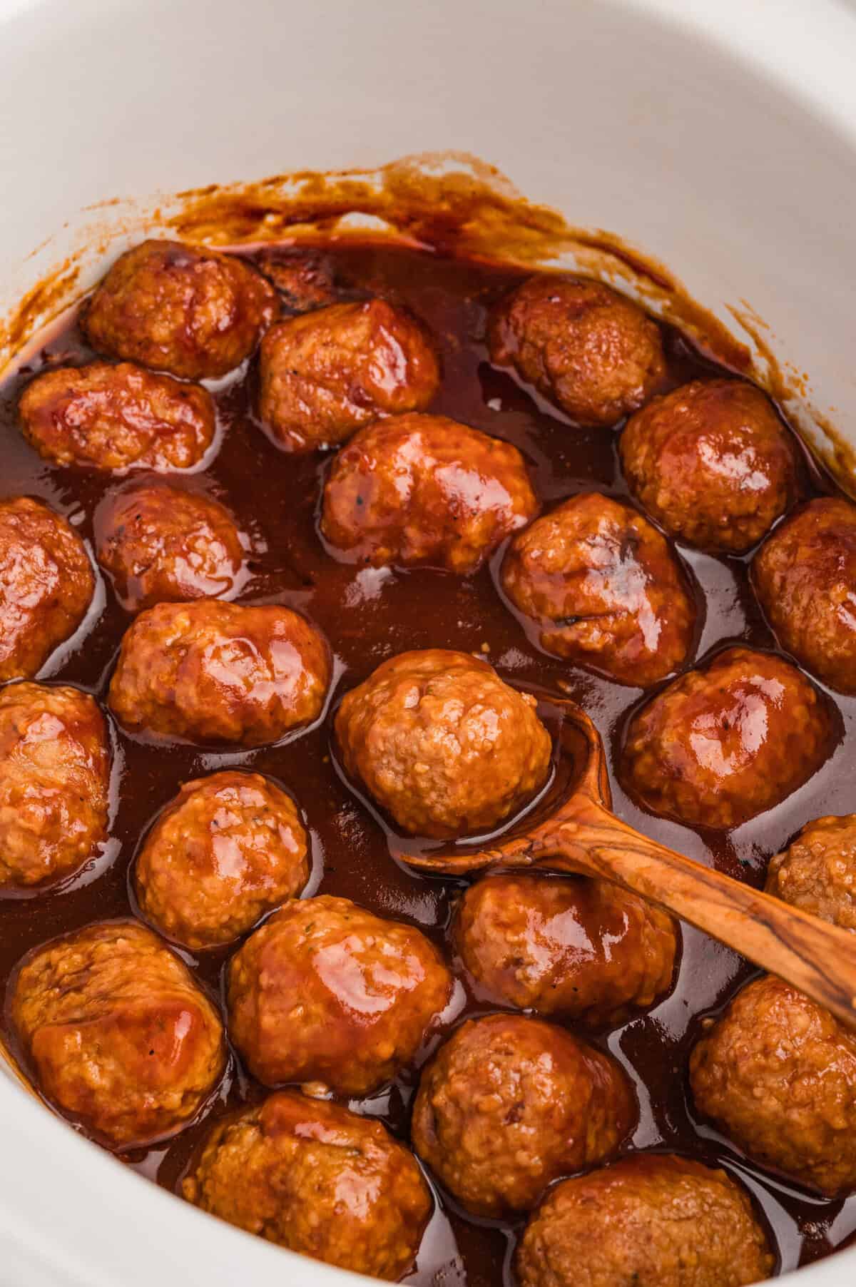 Coca-Cola meatballs in slow cooker with a wooden spoon.