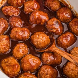 Coca-Cola meatballs in slow cooker with a wooden spoon.