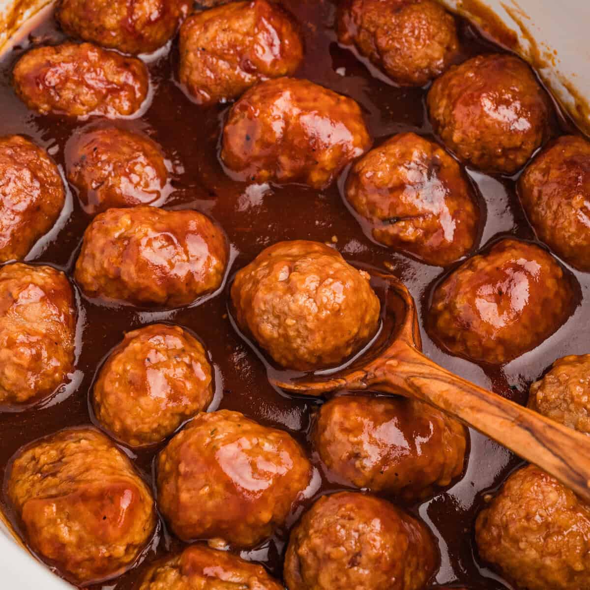 Coca-Cola meatballs in slow cooker with a wooden spoon.
