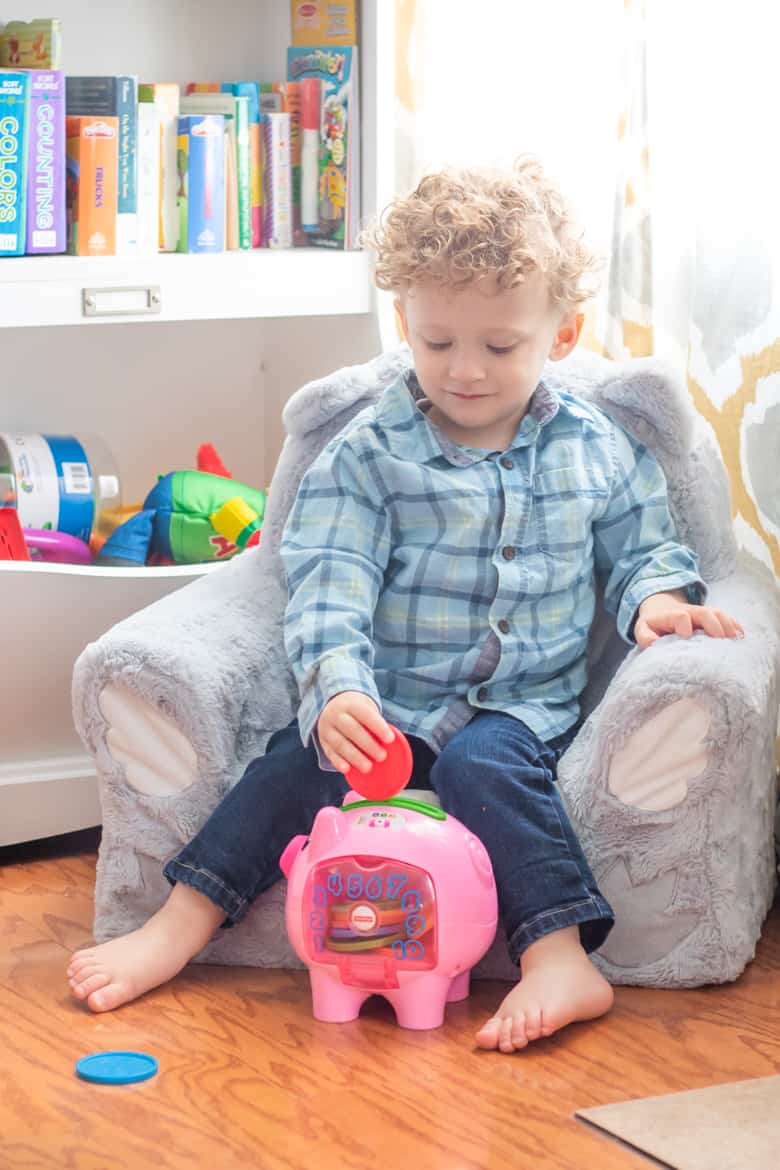 Toddler putting plastic coin in pink piggy bank