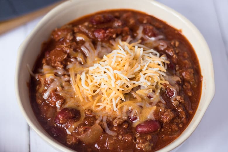 Bowl of beef chili with shredded cheese on top.