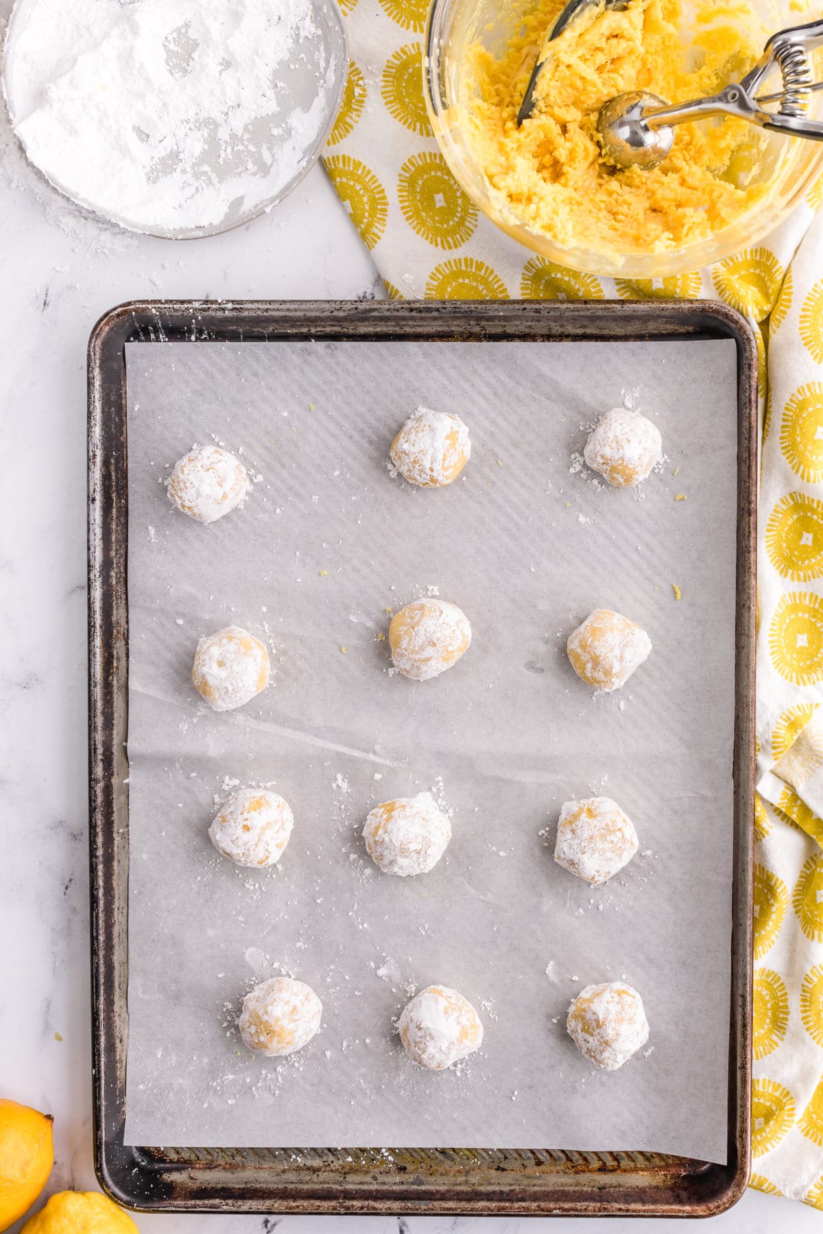 Cookie dough balls coated in powdered sugar on lined baking sheet.