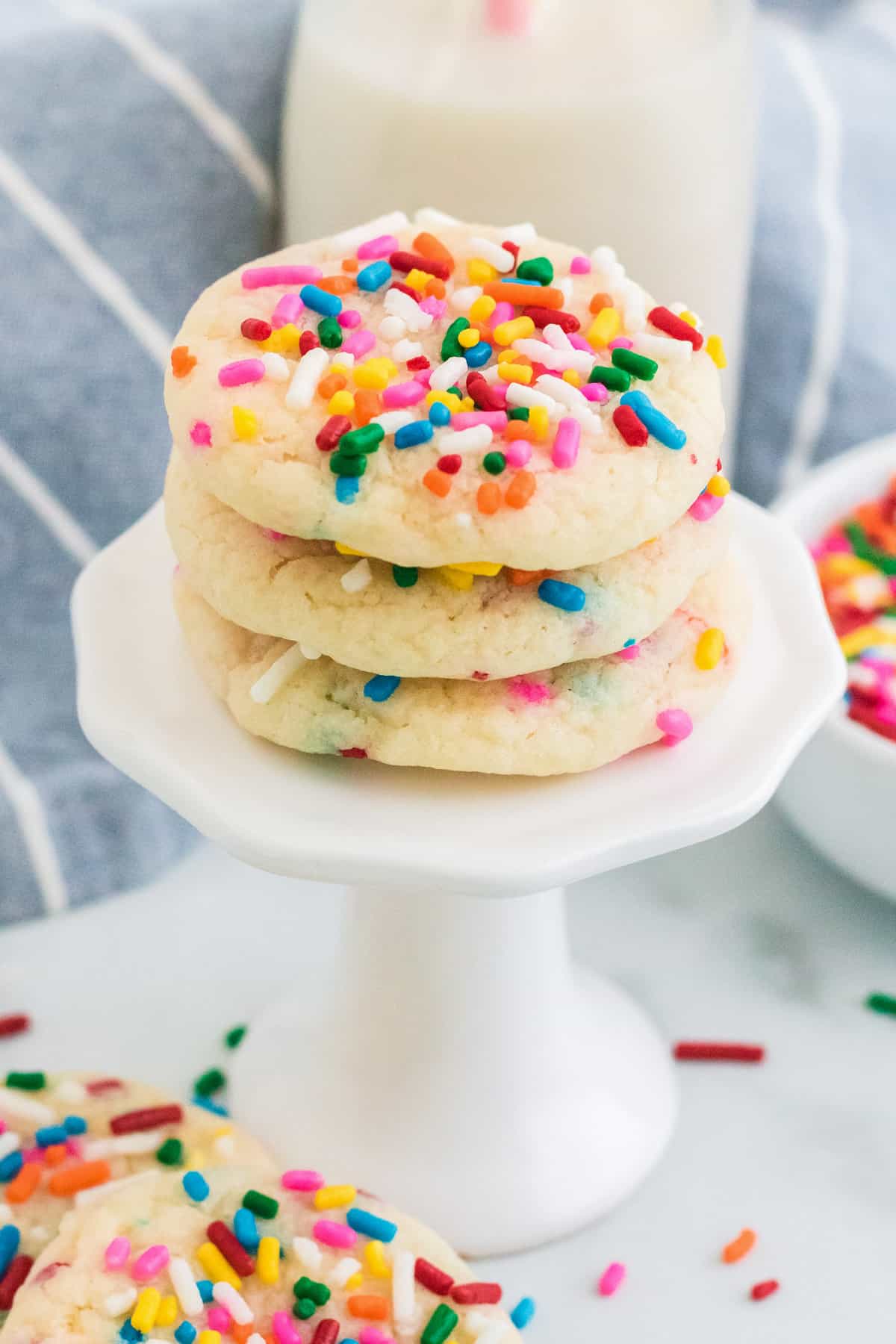 Cake mix funfetti cookies on a cupcake stand next to a cup of milk.