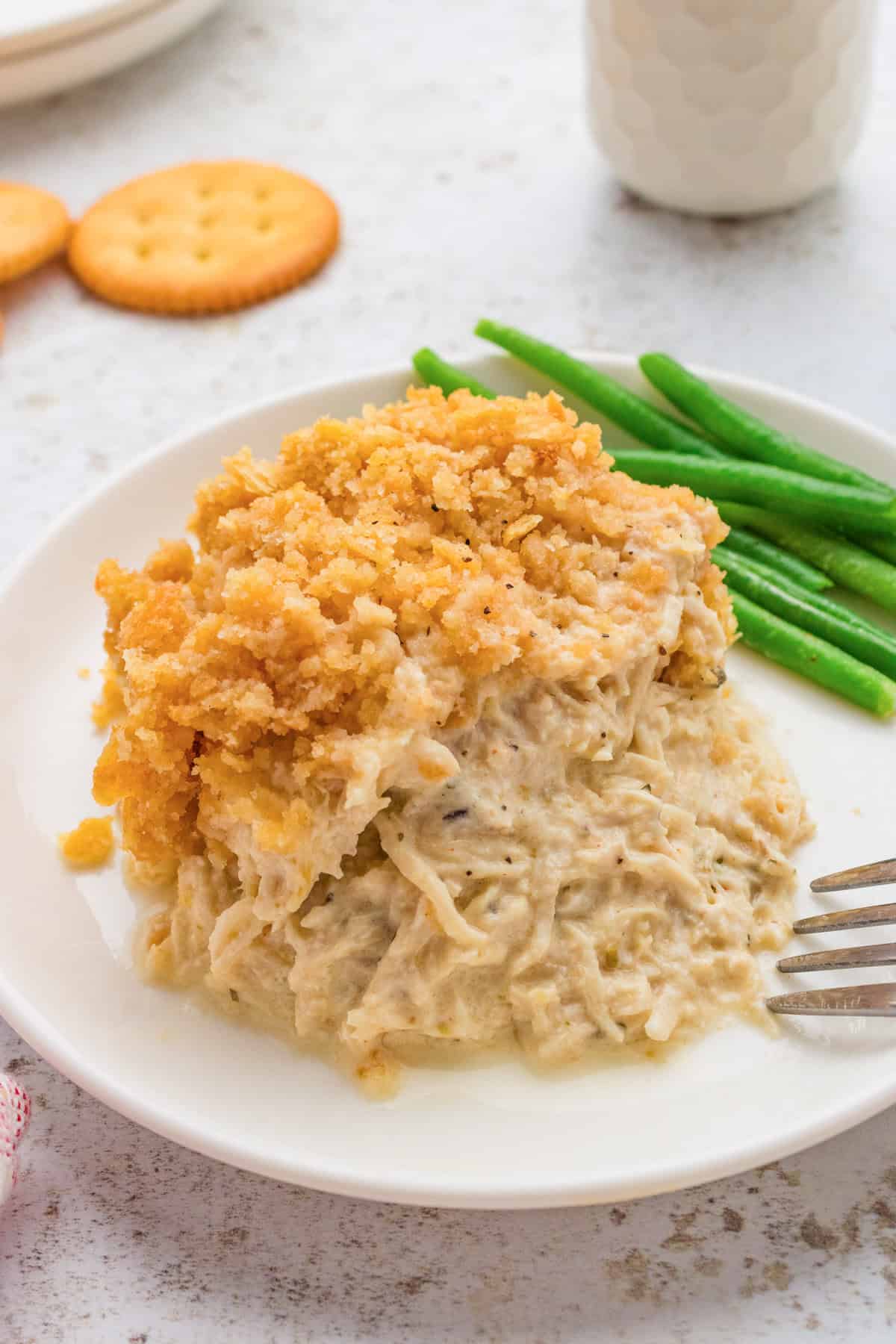 Creamy ritz chicken casserole served with green beans on white plate with ritz crackers and drink in the background.