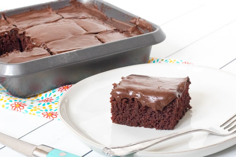 Crazy Wacky Cake in a 9 inch pan sliced into 9 servings. One serving is plated next to the pan.