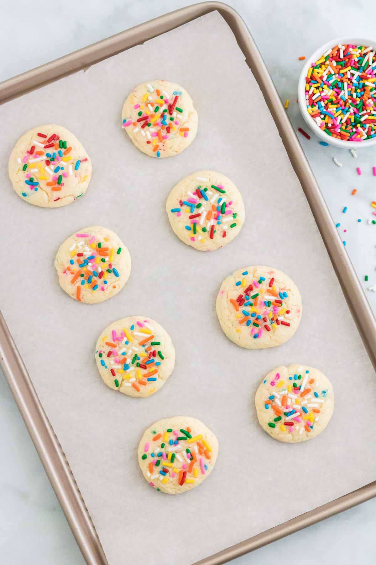 Freshly baked rainbow sprinkle cookies on parchment lined baking sheet.