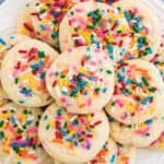 Funfetti cake mix cookies topped with rainbow sprinkles and placed on a white plate for serving.