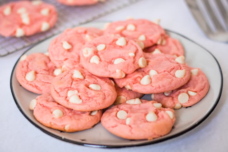 Pink cookies with white chocolate chips stacked on a white plate. 