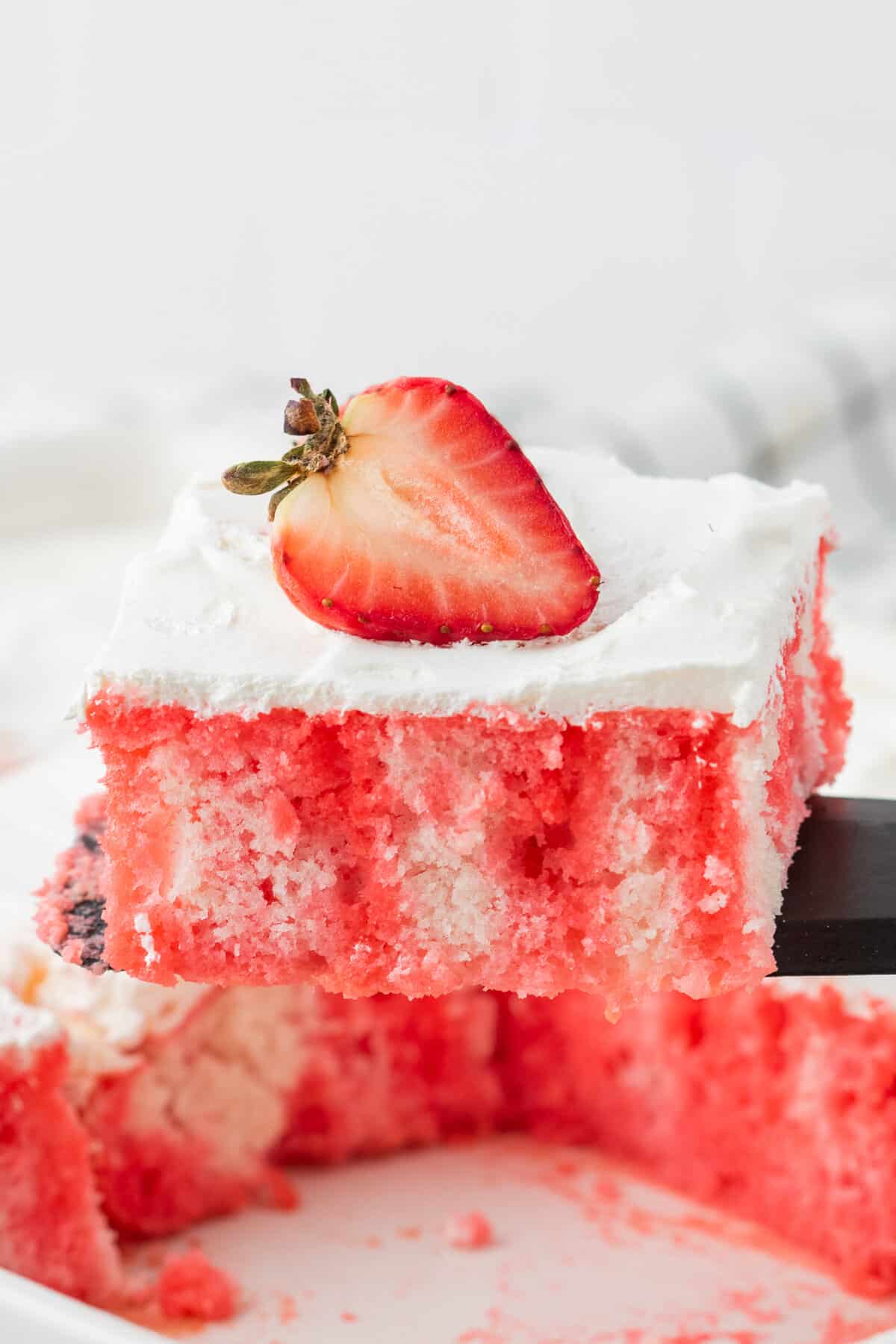 Spatula lifting slice of strawberry jello poke cake from cake dish.