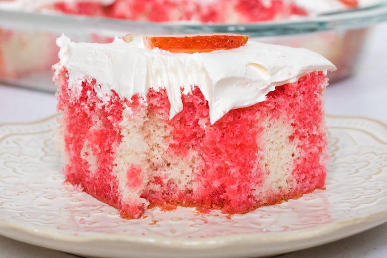 Strawberry Jello Poke Cake with cool whip on white plate with fork marks from a bite that has been taken.