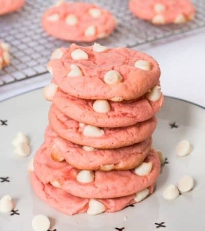 Strawberry cookies with white chocolate chips stacked on top of one another on a plate
