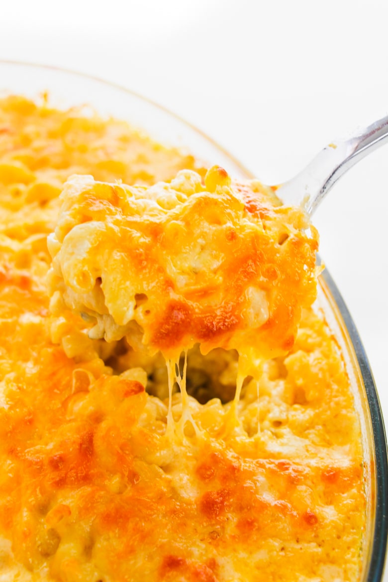 Spoonful of cheesy baked macaroni and cheese coming out of baking dish