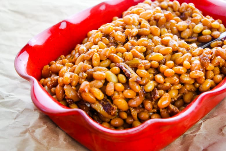 Baked beans with chunks of bacon in red dish.