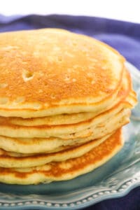 Stack of buttermilk pancakes on a light blue plate with a navy napkin underneath.