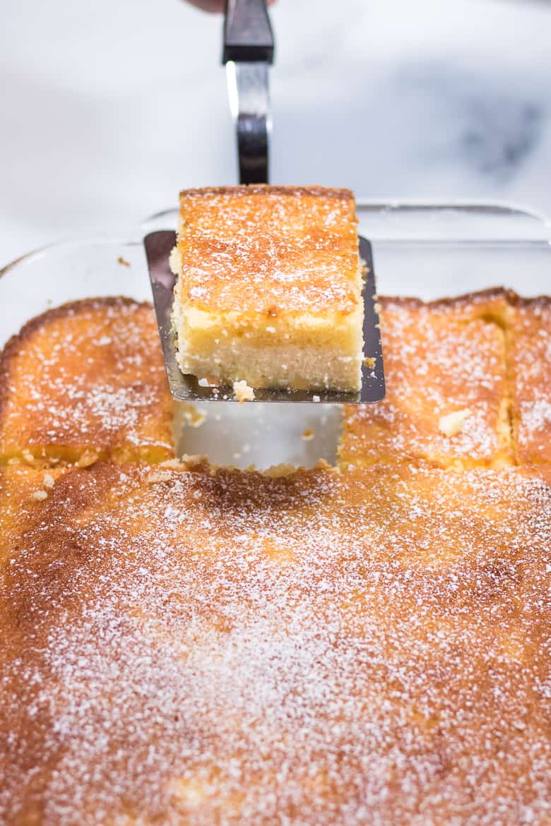 Slice of easy ricotta cake being removed from glass baking dish with spatula.