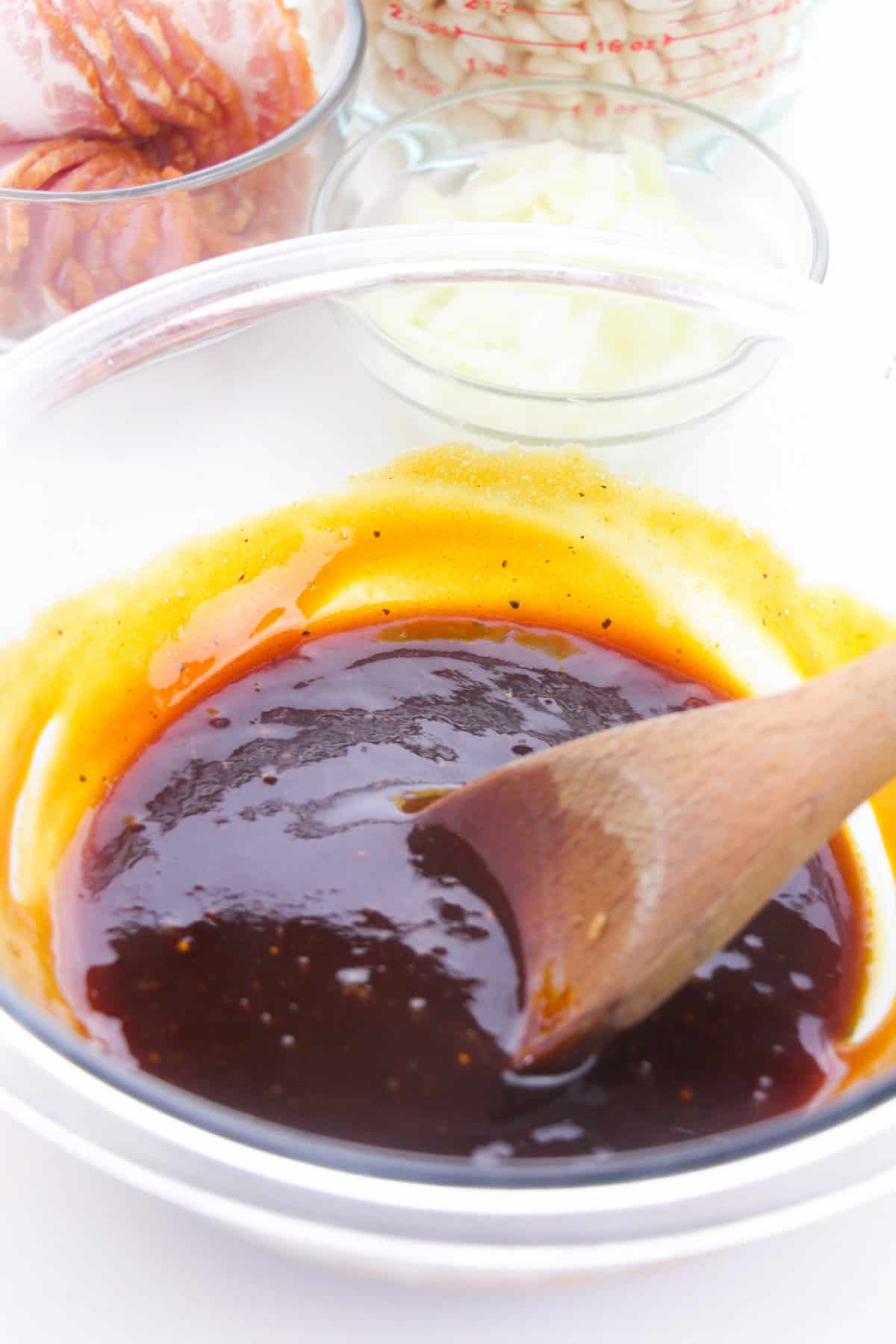Thick, dark brown sauce in a glass bowl with a wooden spoon.