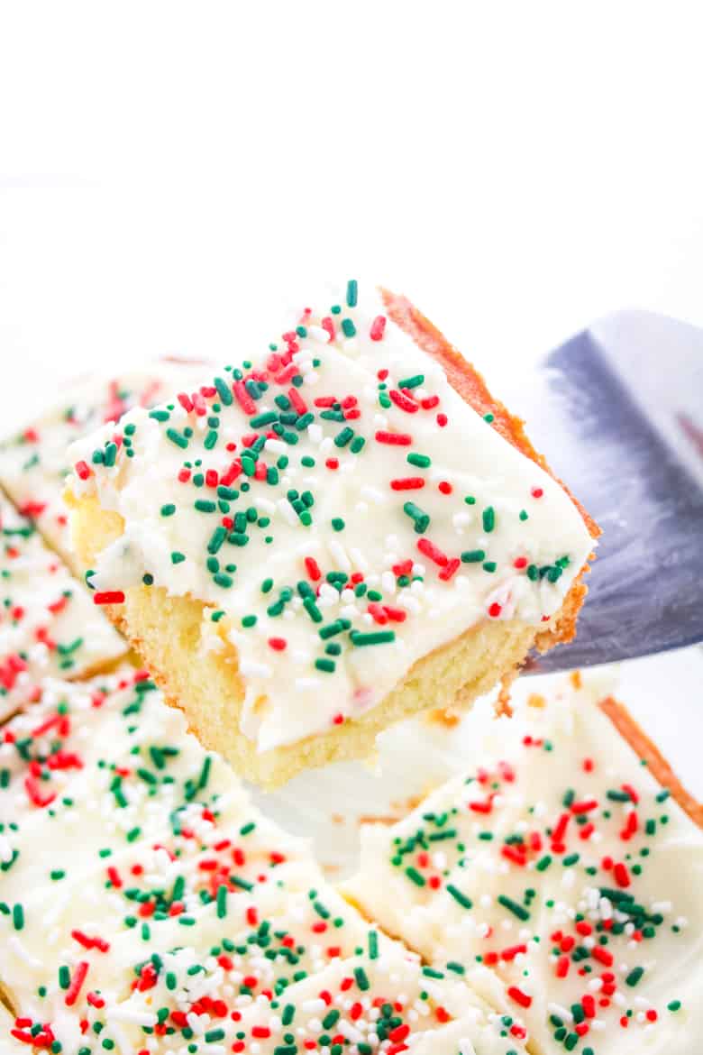 A spatula is serving a slice of vanilla sheet cake with white frosting and red and green sprinkles