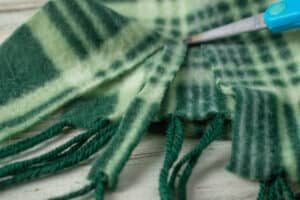 Green plaid scarf being cut into strips with scissors