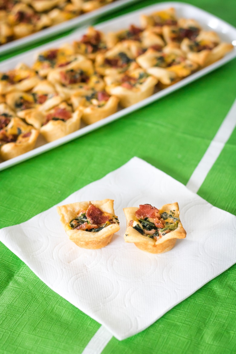 Two bacon spinach dip bites on a napkin with platter of bites in the background