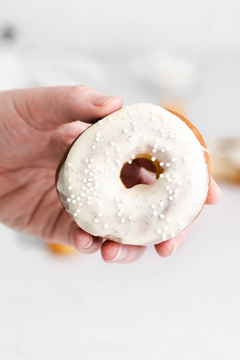 hand holing doughnut with vanilla frosting