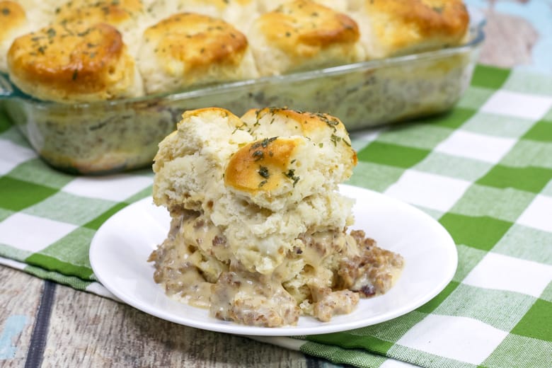 Single serving of biscuits and gravy breakfast casserole on a white plate with 9 x 13 pan of full casserole in background.