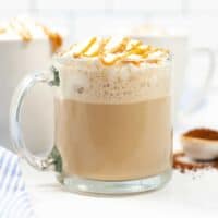 Caramel Macchiato topped with whipped cream and a drizzle of caramel in glass mug