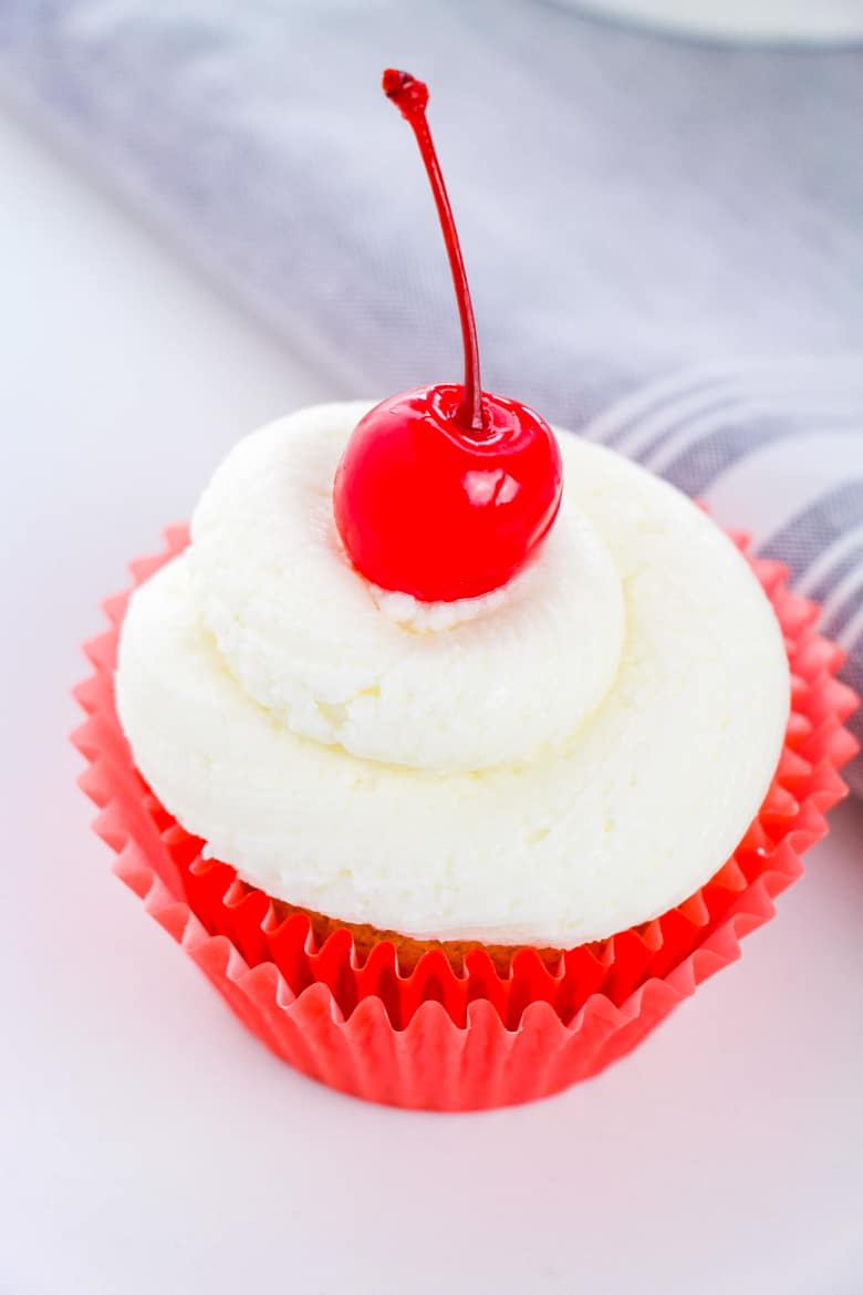 Cupcake in red liner topped with buttercream frosting and cherry