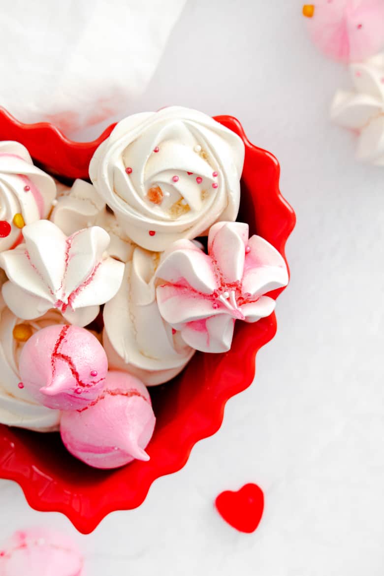 Pink and white meringues decorated with Valentine's Day sprinkles and in a red heart bowl